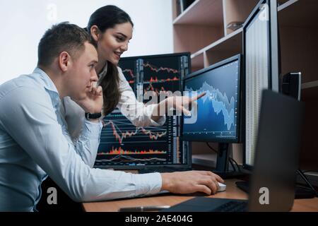 Fille est souriant, guy parle en utilisant le téléphone. Équipe de courtiers en bourse d'une conversation dans un bureau avec plusieurs écrans d'affichage Banque D'Images