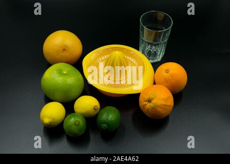 Presse-agrumes jaune avec des oranges, pamplemousses, citrons et limes, le verre vide sur fond noir. Banque D'Images