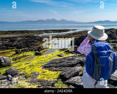 Vacancier Femme regardant à travers les jumelles de Colonsay sur la mer jusqu'à la Paps of Jura, Hébrides intérieures, Ecosse, Royaume-Uni Banque D'Images