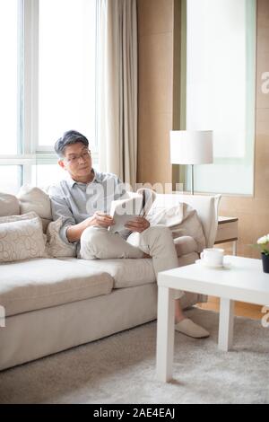 Happy senior man reading book in living room Banque D'Images