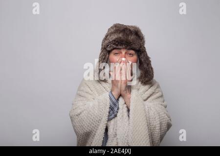 Homme mûr couvrant lui-même avec une couverture et hat soufflant le nez avec un mouchoir. Concept de santé.M Banque D'Images