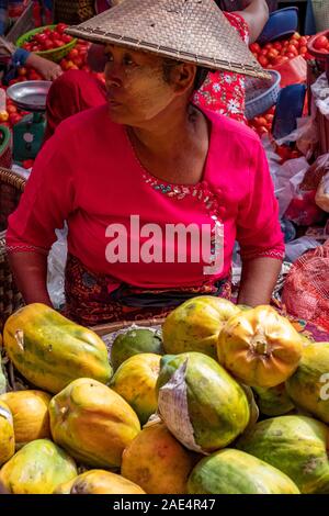 Une femme birmane dans un chemisier rouge et riz conique hat vend des papayes fraîches dans le marché ferroviaire de Mandalay, Myanmar (Birmanie) Banque D'Images