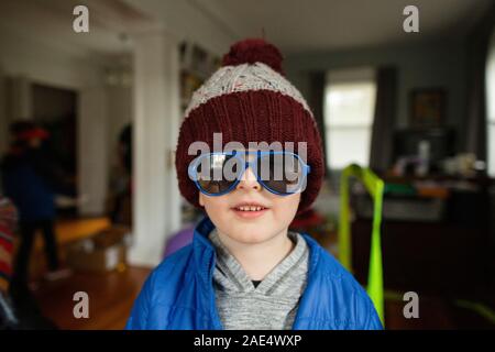 Milieu tourné de boy wearing blue lunettes de soleil et chapeau d'hiver à l'intérieur à la maison Banque D'Images