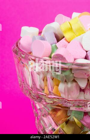 Valentines Day hearts conversation candy vierge dans un voir par le verre cristal. L'arrière-plan est texturée papier rose vif. Banque D'Images