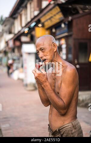 Un vieil homme fume dans la rue du Luang Prabang, Laos, Asie Banque D'Images