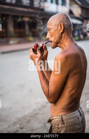 Un vieil homme fume dans la rue du Luang Prabang, Laos, Asie Banque D'Images