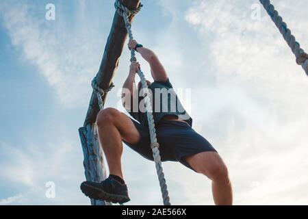Ci-dessous-vue d'un homme fort tirant lui-même une corde contre le ciel bleu Banque D'Images