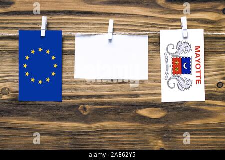 Drapeaux suspendus de l'Union européenne et d'Mayotte attaché à corde avec pinces à linge avec de l'espace de copie sur papier blanc sur fond de bois.rel diplomatique Banque D'Images