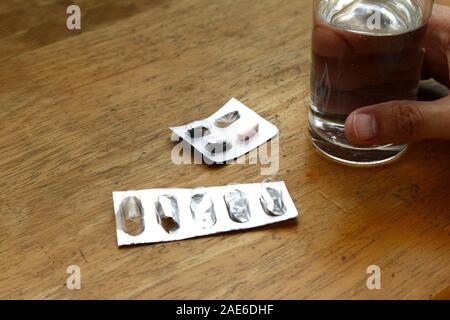 Photo de sachets médecine vide sur une table et main tenant un verre d'eau Banque D'Images