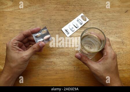 Photo de sachets médecine vide sur une table et main tenant un verre d'eau Banque D'Images