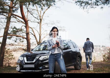 Tasse détient avec boisson chaude. Deux sont arrivés à la forêt sur leur toute nouvelle voiture noir Banque D'Images