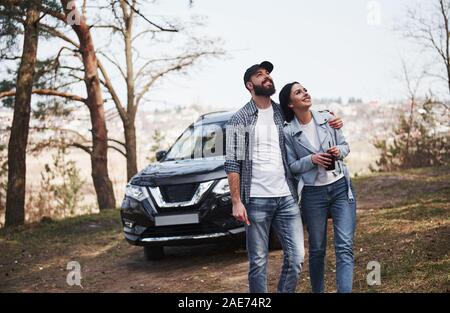 Les personnes positives. Embrassant et profiter de la nature. Deux sont arrivés à la forêt sur leur toute nouvelle voiture noir Banque D'Images