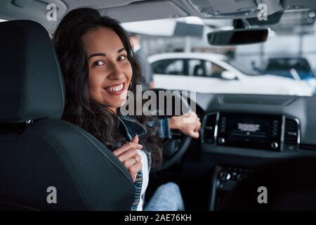 En arrière. ute fille aux cheveux noirs d'essayer son tout nouveau cher voiture dans le salon de l'automobile Banque D'Images