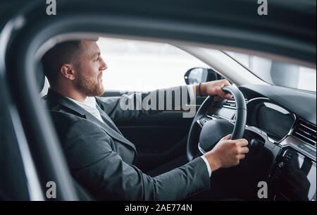 Heureux barbu. Homme d'affaires moderne d'essayer sa nouvelle voiture dans le salon de l'automobile Banque D'Images