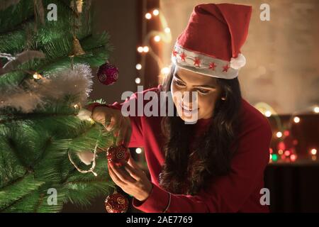 Young woman decorating Christmas Tree à la maison. Banque D'Images