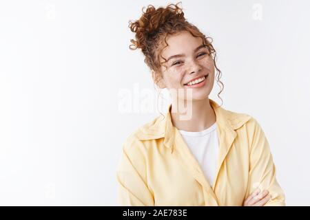 Heureux positif lumineux beau jeune 20s des étudiants de l'université féminine de rousseur rousse chignon désordonné bouclés cross arms poitrine blanc occasionnels posent debout Banque D'Images