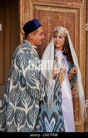 Couples nuptiales en vêtements traditionnels posant devant de la célèbre place du Registan, Samarkand, Ouzbékistan, l'Asie centrale Banque D'Images