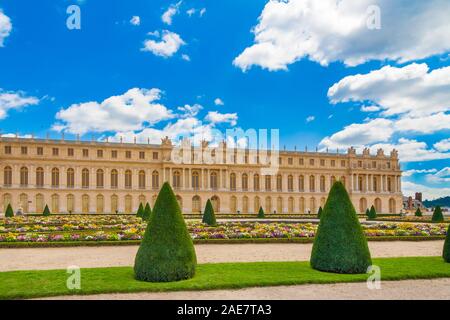 Vue panoramique parfaite de la façade de l'aile sud du château de Versailles avec un sentier de gravier, pelouse, fleurs et arbres en forme de cône, typique de... Banque D'Images