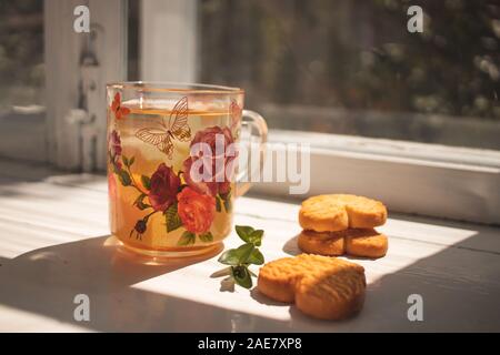 Thé aux herbes. Une tasse en verre avec plateau se tient sur le rebord. Des biscuits en forme de coeur Banque D'Images