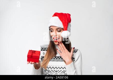 Beautifiul Close up portrait of young woman in red Santa hat on white background studio. Nouveau concept de vacances de Noël année surpris fille mignonne dents Banque D'Images