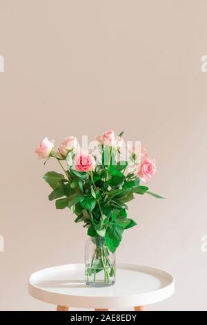 Rose pastel naturelles roses dans un vase en verre sur le tableau blanc sur fond beige lumière Banque D'Images
