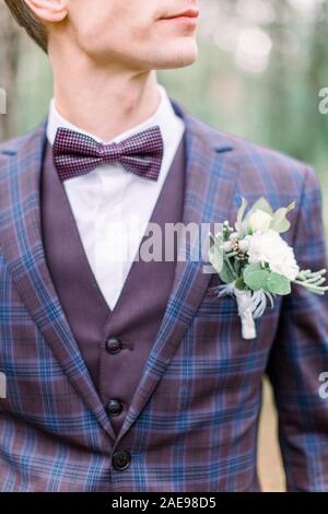 Photo recadrée de la séduisante marié avec papillon dans un costume avec boutonnière sur la veste, debout sur le fond de la forêt. Banque D'Images