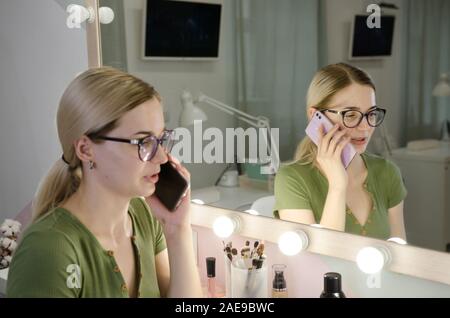 Les jeunes femmes constituent des pourparlers de l'artiste par téléphone avec le client. Styliste professionnel dans sa beauté visage studio Banque D'Images