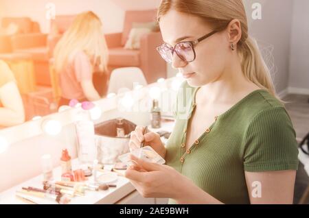 Jolie jeune femme blonde à lunettes faire faire à l'aide d'une palette de cosmétiques Banque D'Images