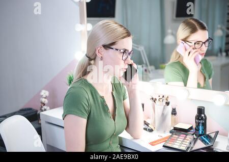 Femme blonde composent artiste parle par téléphone avec le client. Styliste professionnel dans sa beauté visage studio Banque D'Images