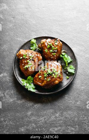 Sucré et épicé de cuisses de poulet grillés au miel sur plaque sur fond noir en noir avec de l'espace texte libre. Une cuisine savoureuse dans un style asiatique. Banque D'Images