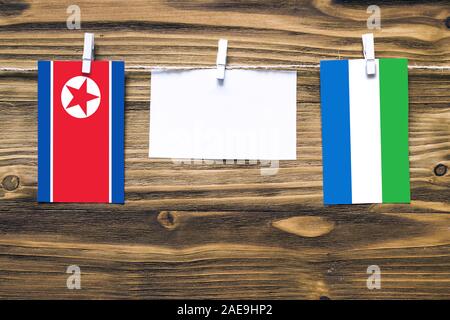 Drapeaux suspendus de la Corée du Nord et en Sierra Leone attaché à corde avec pinces à linge avec de l'espace de copie sur papier blanc sur fond de bois.r diplomatique Banque D'Images