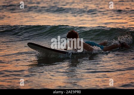 Surfer garçon allongé sur une planche de surf dans la soirée à l'heure du coucher du soleil Banque D'Images