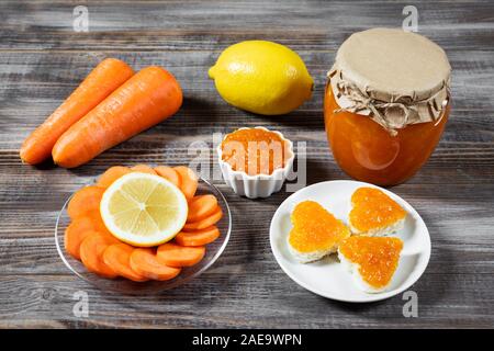 Confiture carotte fait maison avec le citron dans un bocal en verre et bol sur un fond en bois brun foncé. Délicieux toasts en forme de cœur à la carotte de la confiture. Banque D'Images