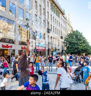 L'homme qui fait des bulles et des enfants qui tentent de capturer les bulles dans la vieille ville de Prague, République tchèque. Banque D'Images