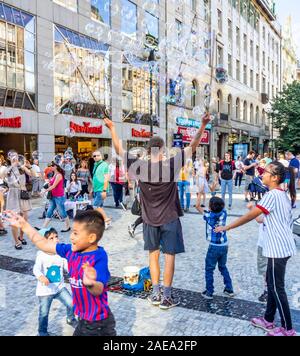 L'homme qui fait des bulles et des enfants qui tentent de capturer les bulles dans la vieille ville de Prague, République tchèque. Banque D'Images