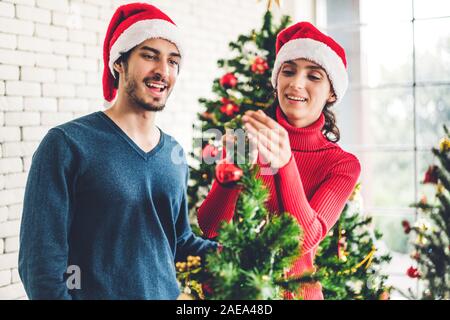 Doux romantique en couple santa hats s'amusant decorating Christmas Tree et souriant tout en célébrant l'nouvel an et profiter de passer du temps togethe Banque D'Images