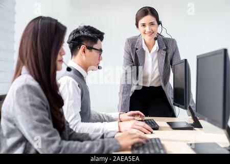 La confiance des jeunes adultes avec superviseur femme debout devant la table de travail de l'agent de l'équipe de l'opérateur avec casques et dans l'ordinateur de bureau Banque D'Images