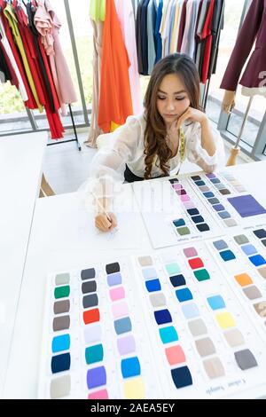 Vue grand angle, un jeune créateur de mode adultes et esquisses de son travail à son atelier avec une palette de couleurs comme l'unique propriétaire. À l'aide d'entre Banque D'Images