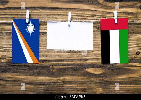 Drapeaux suspendus des Îles Marshall et Emirats Arabes Unis attaché à la corde avec des pinces à linge avec de l'espace de copie sur papier blanc sur fond de bois Banque D'Images