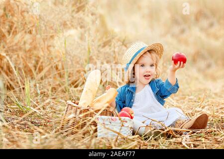 Portrait d'une douce belle petite fille au chapeau de paille dans un champ de blé et est titulaire d'un big red apple dans sa main Banque D'Images