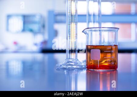 Bécher en verre avec solution orange et carter en bleu fond laboratoire de chimie recherche Banque D'Images