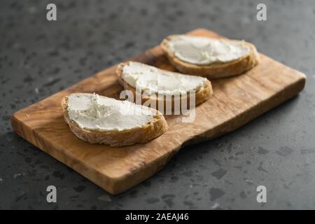 Trois tranches de pain ciabatta avec fromage à la crème sur le bois d'olive sur la surface du sol en terrazzo, accent peu profondes Banque D'Images