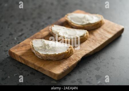 Trois tranches de pain ciabatta avec fromage à la crème sur le bois d'olive sur la surface du sol en terrazzo, accent peu profondes Banque D'Images