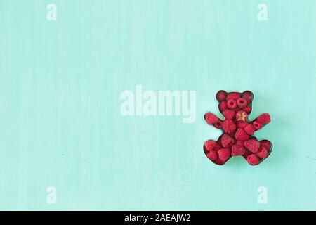 Moule en forme de nounours pour les cookies plein de framboises fraîches sur fond bleu turquoise. Banque D'Images