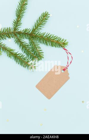 Vue de dessus sur gift tag fabriqué à partir de carte recyclé marron avec string rouge et blanc sur la direction générale de l'épinette sur fond bleu clair. Joyeux Noël. Maison de vacances seaso Banque D'Images