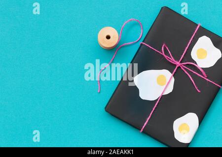 Vue de dessus sur de jolies présents enveloppés dans du papier noir et décoré avec des oeufs clairs sur fond noir avec des ciseaux et ruban rose. Drôle de cadeau pour naissance Banque D'Images