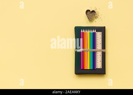 L'école colorés et des fournitures de bureau - crayons et de la règle du livre noir de copeaux en forme de coeur sur fond jaune clair. Vue supérieure avec copie s Banque D'Images