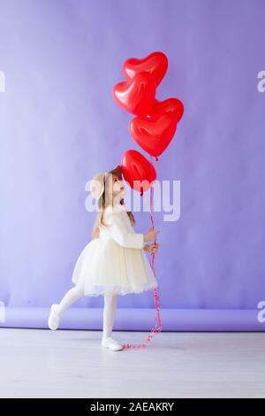Belle petite fille aux ballons rouges en forme de cœur Banque D'Images