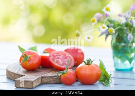 Tomates au basilic frais bio sur planche de bois sur la table dans le jardin aux beaux jours d'été. Concept d'aliments sains. Banque D'Images