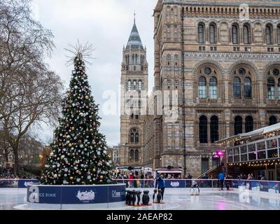 Patinoire à l'extérieur du National History Museum pendant les fêtes de fin d'année, Londres. Les responsables organisent les "pingouins" pour que les enfants puissent les utiliser pour tenir. Banque D'Images